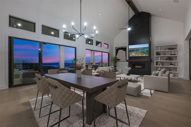 dining space featuring high vaulted ceiling, light hardwood / wood-style floors, beam ceiling, a notable chandelier, and a large fireplace