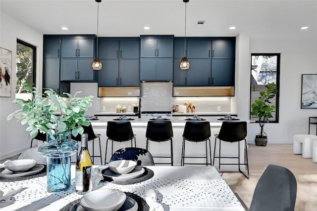 kitchen featuring a kitchen breakfast bar, backsplash, a kitchen island with sink, pendant lighting, and light hardwood / wood-style floors