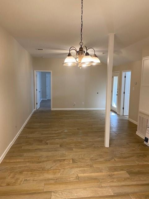 unfurnished dining area with wood-type flooring and an inviting chandelier