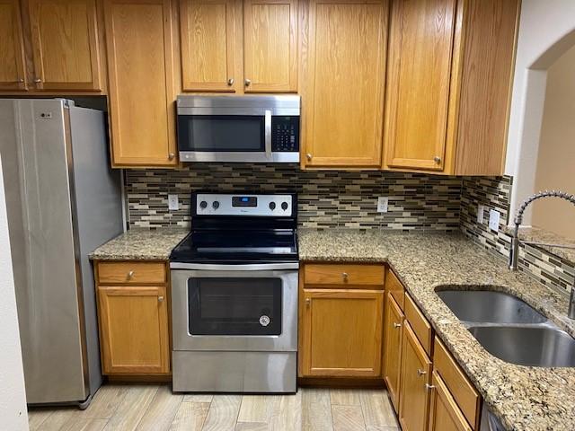 kitchen with light stone countertops, appliances with stainless steel finishes, light wood-type flooring, tasteful backsplash, and sink