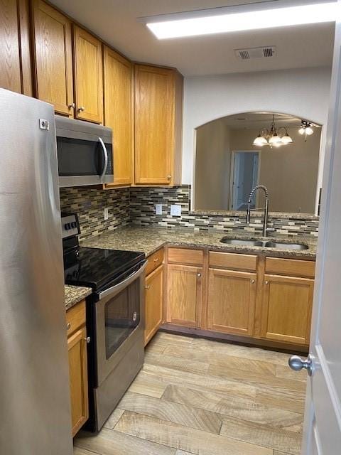 kitchen featuring light wood-type flooring, tasteful backsplash, stainless steel appliances, sink, and a notable chandelier