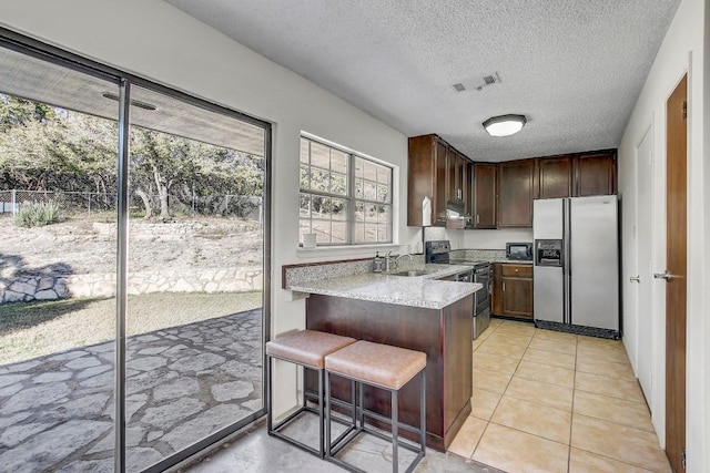 kitchen featuring kitchen peninsula, appliances with stainless steel finishes, a textured ceiling, and a kitchen breakfast bar