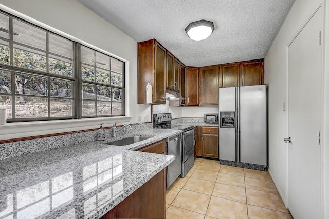 kitchen with sink, a textured ceiling, appliances with stainless steel finishes, light tile patterned flooring, and light stone counters