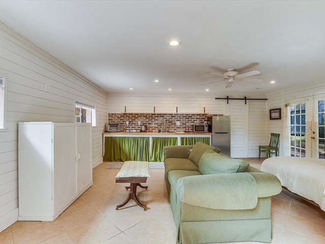 living room featuring ceiling fan, a barn door, light tile patterned floors, and sink