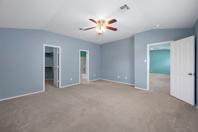 unfurnished bedroom with a walk in closet, connected bathroom, a closet, vaulted ceiling, and ceiling fan