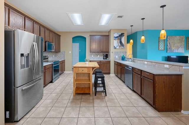 kitchen with kitchen peninsula, hanging light fixtures, a center island, decorative backsplash, and stainless steel appliances