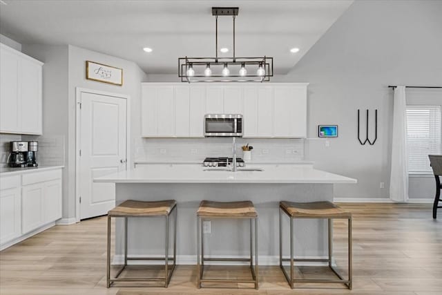 kitchen featuring pendant lighting, a center island with sink, light hardwood / wood-style flooring, tasteful backsplash, and white cabinetry