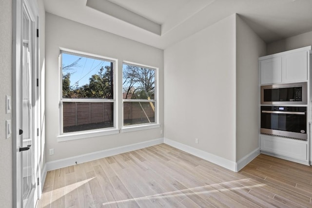 interior space with light wood-type flooring and a tray ceiling