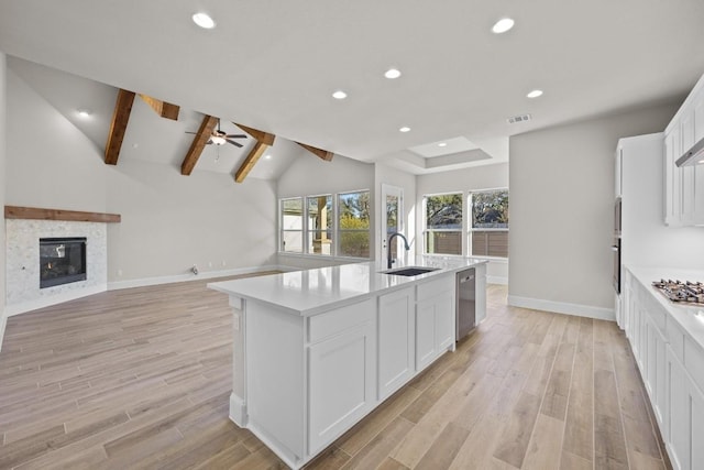 kitchen featuring a center island with sink, sink, vaulted ceiling with beams, light wood-type flooring, and white cabinetry