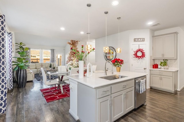 kitchen featuring pendant lighting, dishwasher, dark wood-type flooring, sink, and an island with sink