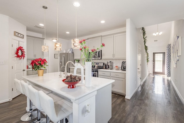 kitchen featuring pendant lighting, dark wood-type flooring, gray cabinets, an island with sink, and stainless steel appliances