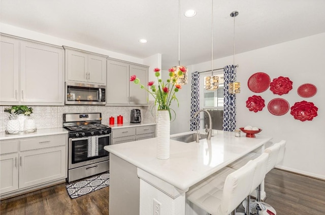 kitchen featuring a kitchen island with sink, a sink, hanging light fixtures, appliances with stainless steel finishes, and light countertops