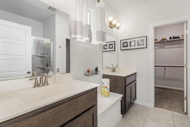 bathroom featuring two vanities, visible vents, a spacious closet, a stall shower, and a sink