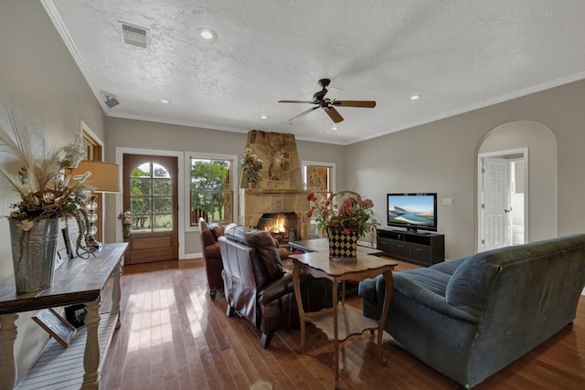 living room featuring a stone fireplace, ornamental molding, and dark wood-type flooring