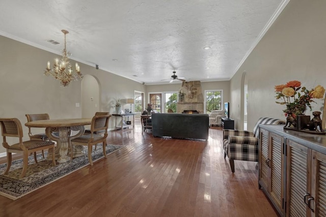 living room with ceiling fan with notable chandelier, a stone fireplace, dark hardwood / wood-style flooring, and ornamental molding