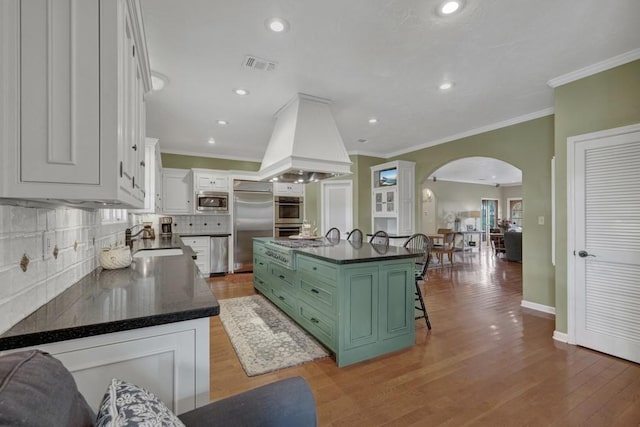 kitchen featuring white cabinetry, a center island, built in appliances, light wood-type flooring, and green cabinetry