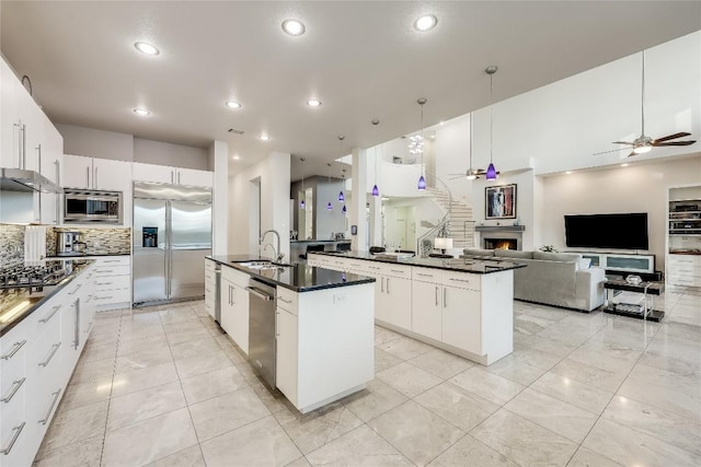 7302 Matisse Pointe Dr, Jonestown, TX 78645 - kitchen with built in appliances, a center island with sink, dark countertops, a sink, and ceiling fan