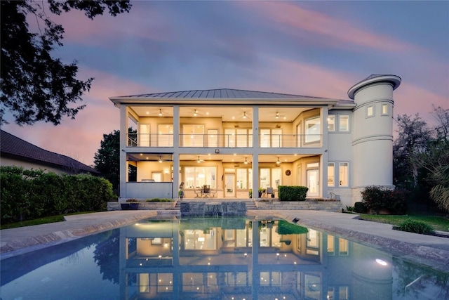 back house at dusk featuring a balcony, ceiling fan, and a patio