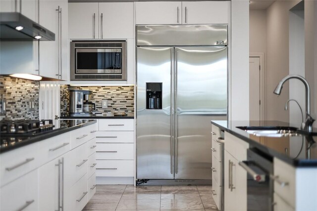 7302 Matisse Pointe Dr, Jonestown, TX 78645 - kitchen featuring built in appliances, a sink, dark countertops, light marble finish floors, and under cabinet range hood