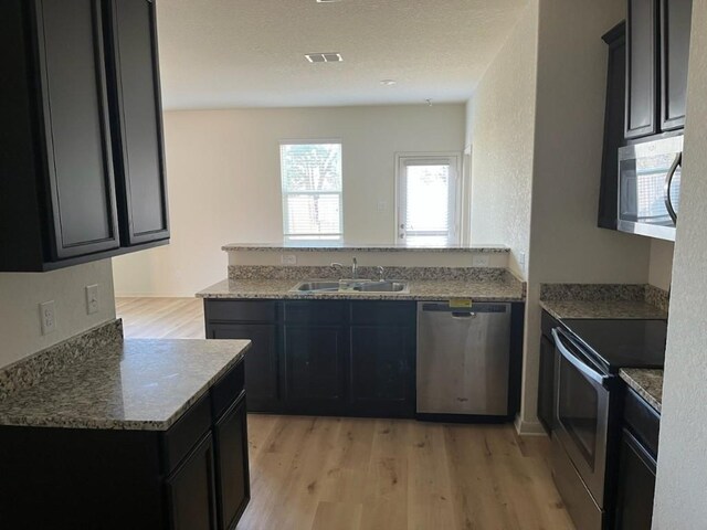 kitchen featuring kitchen peninsula, stainless steel appliances, sink, stone countertops, and light hardwood / wood-style floors