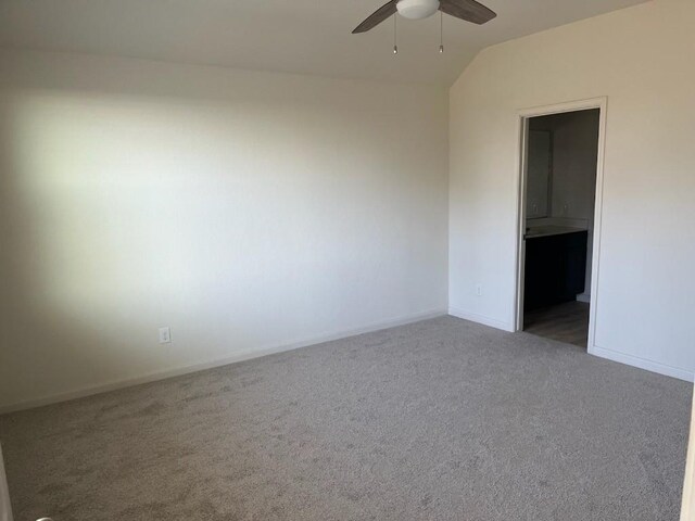 spare room with dark colored carpet, vaulted ceiling, and ceiling fan