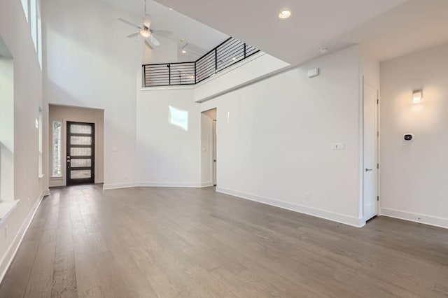 unfurnished living room featuring a high ceiling, dark hardwood / wood-style flooring, and ceiling fan