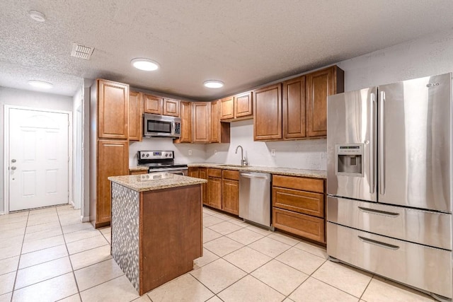 kitchen with a center island, sink, light tile patterned floors, a textured ceiling, and appliances with stainless steel finishes