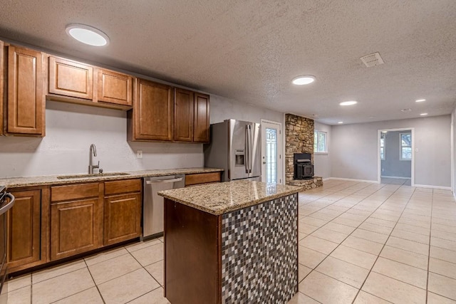 kitchen with a wood stove, sink, stainless steel appliances, a textured ceiling, and light tile patterned floors