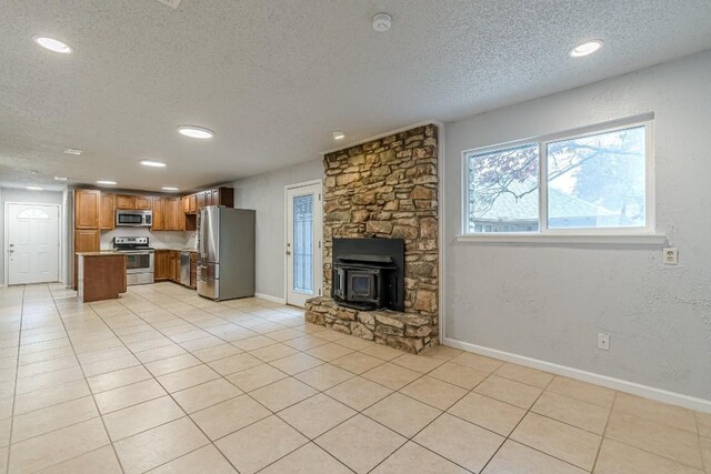 kitchen with a textured ceiling, light tile patterned flooring, a wood stove, and stainless steel appliances