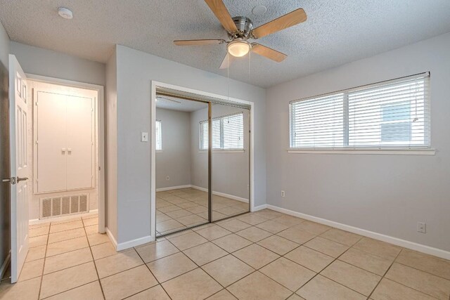 unfurnished bedroom with ceiling fan, a closet, light tile patterned flooring, and a textured ceiling