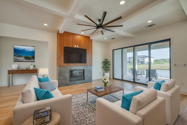 living room featuring beamed ceiling, wood-type flooring, a tile fireplace, and ceiling fan