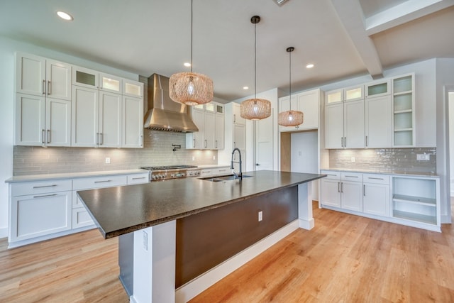 kitchen featuring decorative backsplash, a kitchen island with sink, sink, and wall chimney range hood