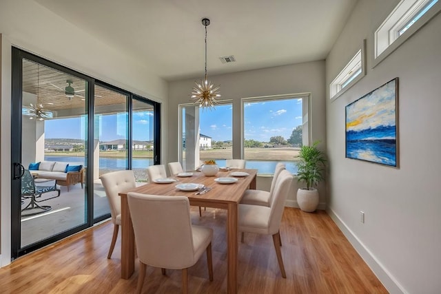 dining area with ceiling fan with notable chandelier, a water view, and light hardwood / wood-style flooring