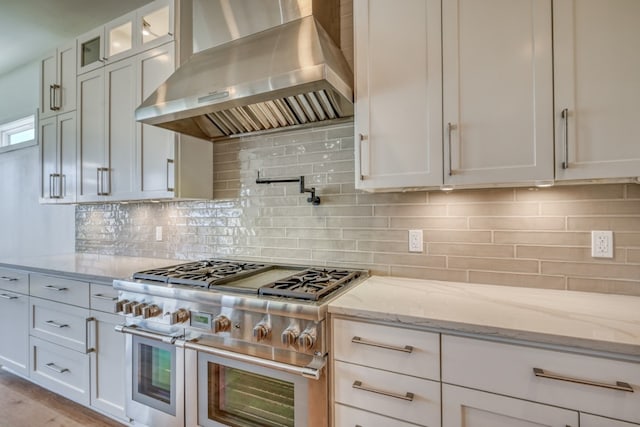 kitchen with white cabinetry, wall chimney exhaust hood, light stone countertops, and range with two ovens