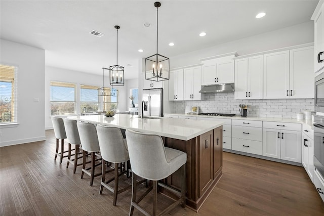 kitchen with sink, pendant lighting, white cabinets, a breakfast bar area, and an island with sink