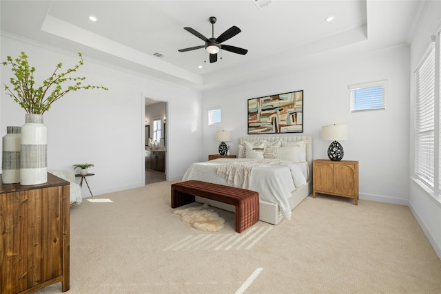 bedroom featuring ceiling fan, ensuite bathroom, light colored carpet, a tray ceiling, and ornamental molding