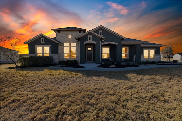 view of front facade with a front yard, stone siding, and stucco siding