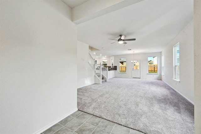 unfurnished living room featuring ceiling fan with notable chandelier and light colored carpet