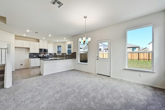 kitchen with kitchen peninsula, appliances with stainless steel finishes, light carpet, decorative light fixtures, and white cabinetry