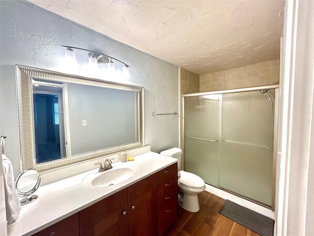 bathroom featuring hardwood / wood-style floors, vanity, a shower with shower door, and toilet