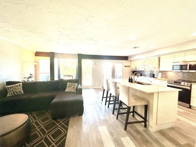 kitchen with electric stove, sink, light wood-type flooring, an island with sink, and plenty of natural light