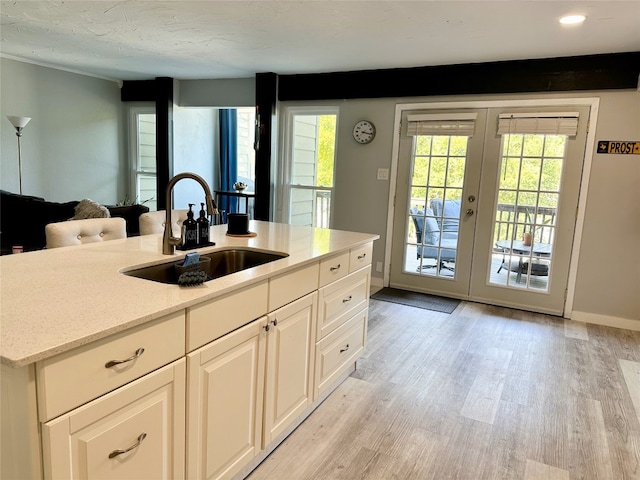 kitchen with light hardwood / wood-style floors, white cabinetry, sink, and an island with sink