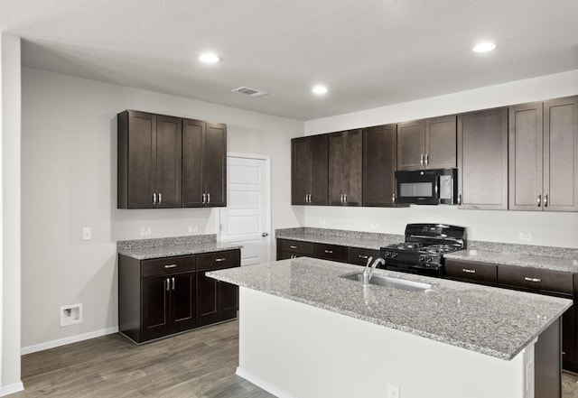 kitchen featuring a kitchen island with sink, sink, light stone counters, and black appliances