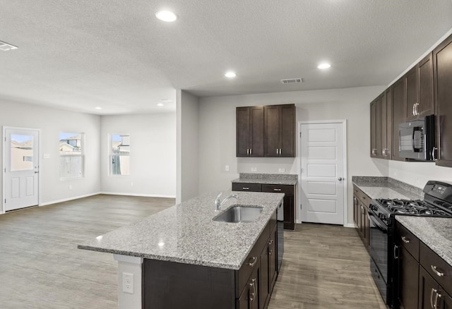 kitchen with wood-type flooring, an island with sink, sink, dark brown cabinetry, and black appliances