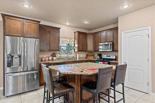 kitchen with a center island, sink, light stone countertops, appliances with stainless steel finishes, and light tile patterned flooring