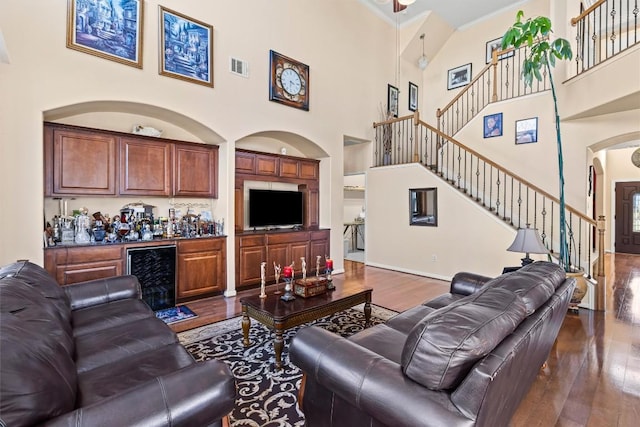 living room with a towering ceiling, beverage cooler, indoor bar, built in features, and hardwood / wood-style floors