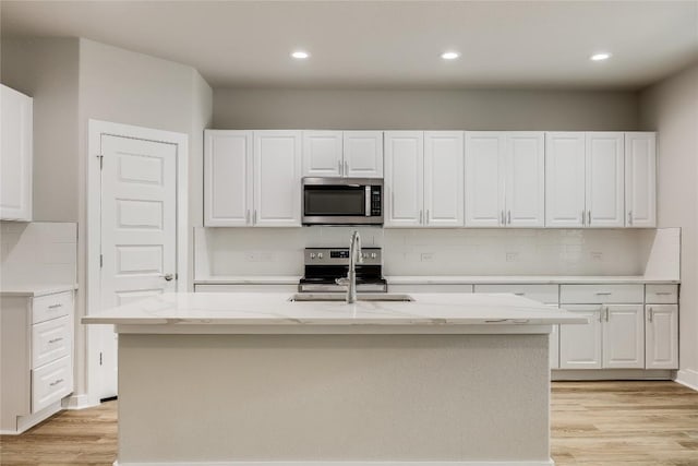 kitchen with white cabinets, stainless steel appliances, a kitchen island with sink, and sink