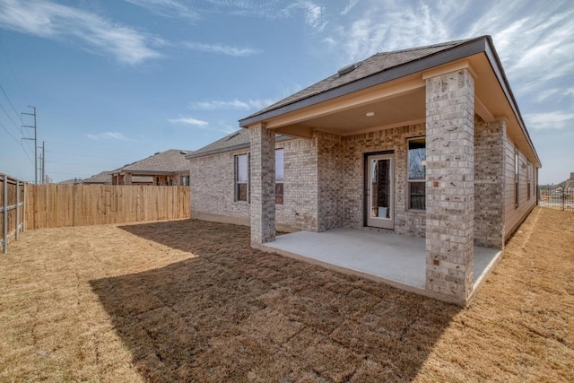 rear view of property with brick siding, a fenced backyard, a lawn, and a patio