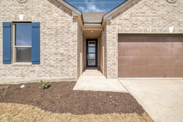 doorway to property featuring a shingled roof, concrete driveway, brick siding, and an attached garage