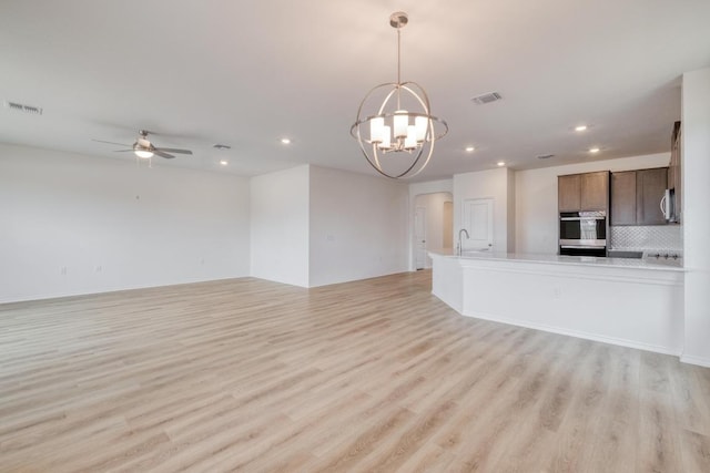 unfurnished living room featuring light wood-style floors, visible vents, arched walkways, and ceiling fan with notable chandelier